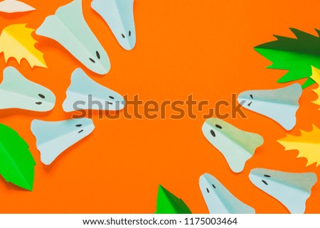 Ghosts and autumn leaves on orange background with space for text. Minimal flat lay. Creative Halloween concept. Spooky and horror. Trick or treat. Cut from paper with handmade. 