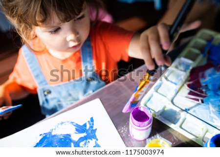 Adorable little kid girl holding paint brushes, painting picrure at the paper. Artistic preschooler, art for children
