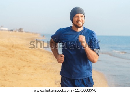 portrait of running smiling man in sportswear and hat against sea background