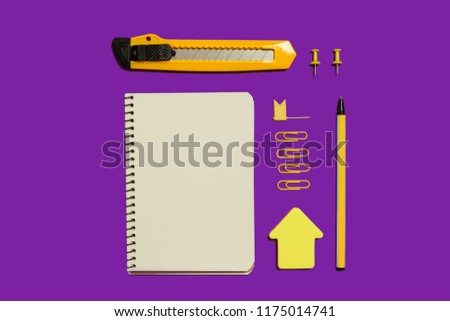opened notebook, colorful stickers, paper clips, pen and stationary knife lying on a purple surface. concept of educational chancery