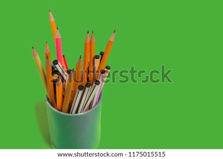 new bright colored pens and pencils standing in a penholder on a green background. concept of office supplies. free copyspace