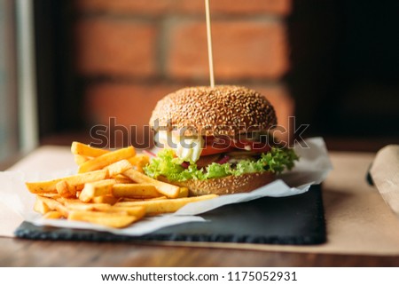 Large tasty burger with French fries in a cafe on a black tray