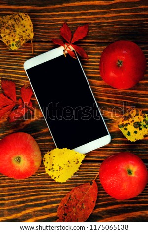 Mock up, smartphone with red apples with yellow and red autumn leaves on wooden brushed background