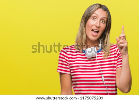 Young beautiful woman listening music wearing headphones over isolated background pointing finger up with successful idea. Exited and happy. Number one.