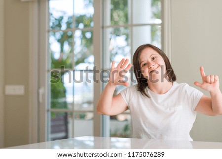 Down syndrome woman at home showing and pointing up with fingers number seven while smiling confident and happy.