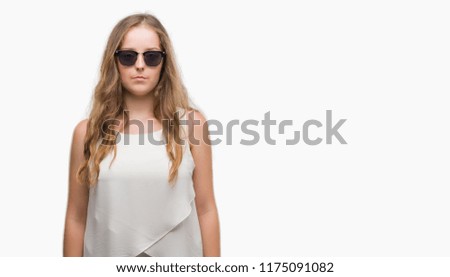 Young blonde woman wearing sunglasses with serious expression on face. Simple and natural looking at the camera.