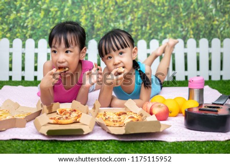 Asian Chinese little sisters eating pizza at outdoor garden