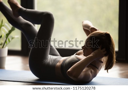 Young sporty woman practicing fitness, doing crisscross exercise, bicycle crunches, working out, wearing sportswear, grey pants and top, indoor full length, yoga studio. Weight loss, slimming concept