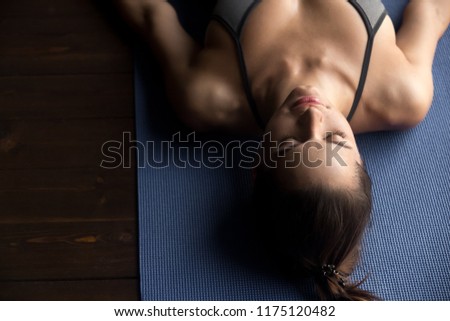 Young sporty woman practicing yoga, doing Dead Body, Savasana exercise, Corpse pose, working out, wearing sportswear, grey top, indoor close up, yoga studio, top view Royalty-Free Stock Photo #1175120482
