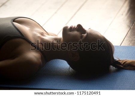 Young sporty woman practicing yoga, doing Dead Body, Savasana exercise, Corpse pose, working out, wearing sportswear, grey top, indoor close up, yoga studio Royalty-Free Stock Photo #1175120491