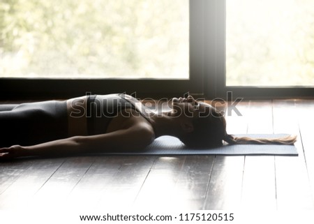Young sporty woman practicing yoga, doing Dead Body, Savasana exercise, Corpse pose, working out, wearing sportswear, grey pants and top, indoor close up, yoga studio Royalty-Free Stock Photo #1175120515