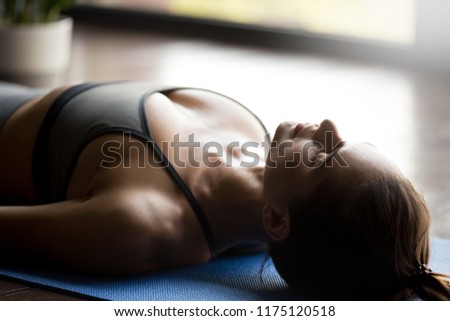 Young sporty attractive woman practicing yoga, doing Dead Body, Savasana exercise, Corpse pose, working out, wearing sportswear, grey top, indoor, face and body close up view, yoga studio Royalty-Free Stock Photo #1175120518
