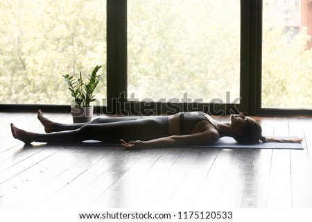 Young sporty woman practicing yoga, doing Dead Body, Savasana exercise, Corpse pose, working out, wearing sportswear, grey pants and top, indoor full length, yoga studio Royalty-Free Stock Photo #1175120533