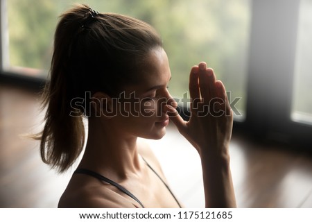 Young attractive woman practicing yoga, doing Alternate Nostril Breathing exercise, nadi shodhana pranayama pose, working out, indoor close up, yoga studio, side view. Mindful healthy life concept Royalty-Free Stock Photo #1175121685
