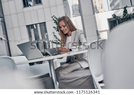 Developing new project. Beautiful young woman using digital tablet and smiling while sitting in the modern restaurant     
