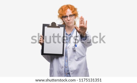 Young redhead doctor woman holding clipboard with open hand doing stop sign with serious and confident expression, defense gesture