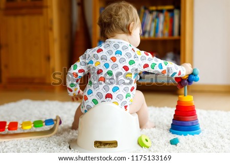 Closeup of cute little 12 months old toddler baby girl child sitting on potty. Kid playing with educational wooden toy. Toilet training concept. Baby learning, development steps Royalty-Free Stock Photo #1175133169