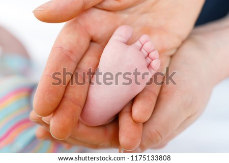 Father or mother holding foot of newborn baby. Adult hand and baby tiny baby feet. Happy parenthood, carefree childhood, family, love, tenderness