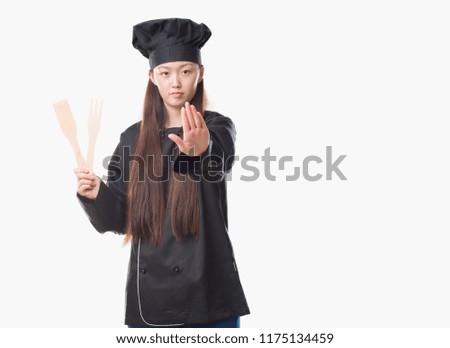 Young Chinese woman over isolated background wearing chef uniform with open hand doing stop sign with serious and confident expression, defense gesture