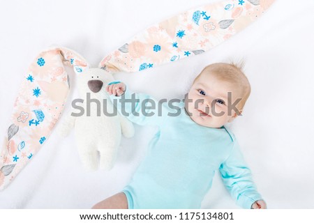Close-up of adorable cute newborn baby girl of two months on white background. Lovely child playing with plush rabbit toy wigh bit long ears. Holiday, Easter, childhood concept