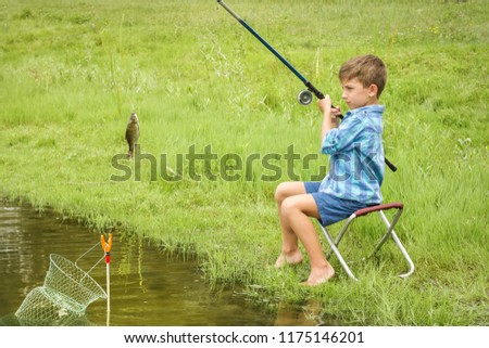 Focused, serious, attentive little boy catch a fish on the river by a fishing rod.