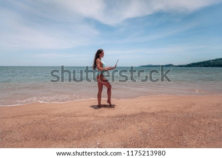 Young successful business woman or student in swimsuit  using laptop in the beach. Working outdoors on seescape background. Mobile Office concept