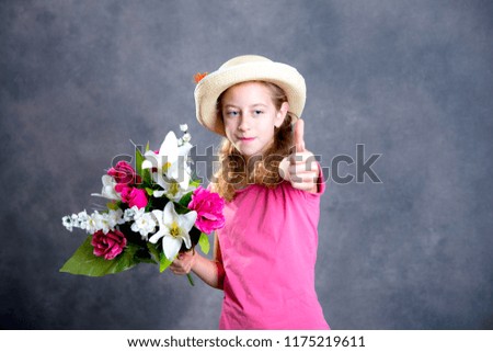 nice blond girl with straw hat, bouquet of flowers and thumb up in front of gray background