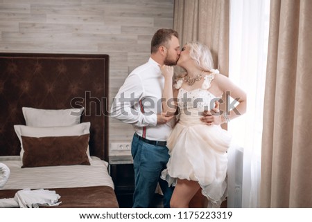 Beautiful newlyweds kissing near the window in the bedroom . The groom and the bride in a lace dress.