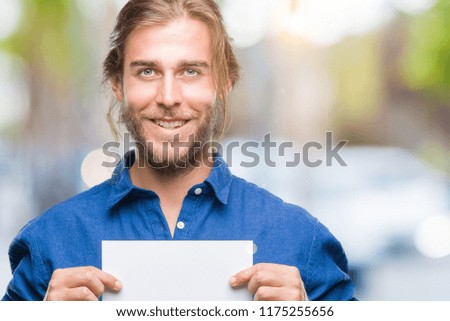 Young handsome man with long hair over isolated background holding blank paper with a happy face standing and smiling with a confident smile showing teeth