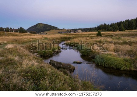 Evening view on the mountain landscape with the dominant hill and large meadow and brook. The area "Jizerské hory" hamlet "Jizerka". Royalty-Free Stock Photo #1175257273