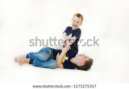 Emotional portrait of two happy and energetic little brothers playing and tickling each other lying on the floor and isolated on white background. Lifestyle concept. Happy childhood. Positive life