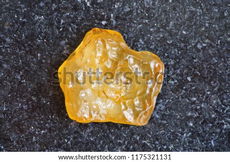 Yellow tektite specimen on dark granite background close-up. Libyan desert glass