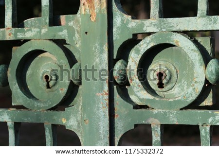 Close up outdoor view of a rusty keyhole of an ancient metallic gate. Green painted surface with circular decorative elements. Vintage image of a weathered steel door. Abstract picture. 