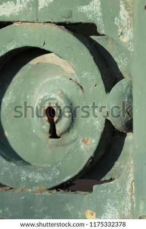 Close up outdoor view of a rusty keyhole of an ancient metallic gate. Green painted surface with circular decorative elements. Vintage image of a weathered steel door. Abstract picture. 