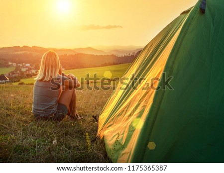 Happy woman with open arms sitting near tent around mountains under sunset light sky enjoying the  leisure and freedom.