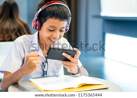Asian happy cute young boy student study in school library He using smartphone wearing headphones play game or learning lesson online class room exam Back to school education concept have copy space