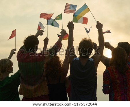 Silhouettes of people holding flags from various countries. Evening sky background.