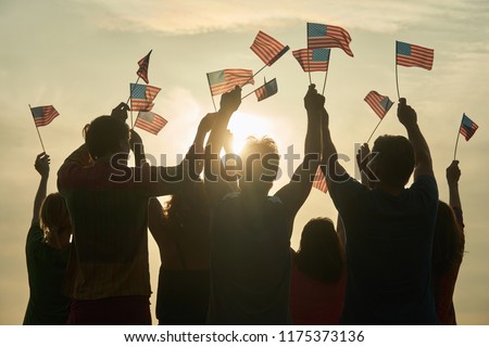 Group of people waving American flags. Silhouette of people with usa flags against evening sunny sky background.