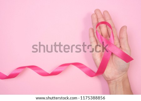 women hand holding pink ribbon breast cancer on pink background. with copy space