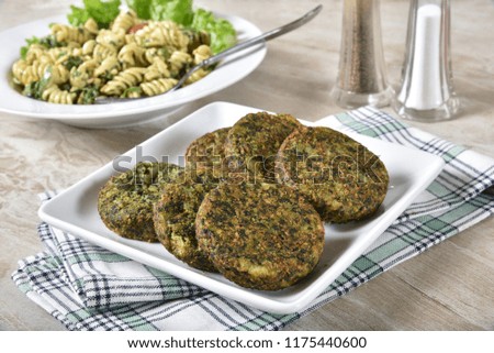 Serving palet of spinach cakes with a bowl of pasta salad in the background