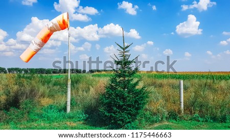 red-white wind direction on the blue sky background on the aerodrome, green field and clouds