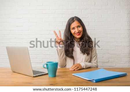 Young indian woman at the office fun and happy, positive and natural, doing a gesture of victory, peace concept