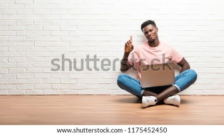 Afro american man sitting on the floor with his laptop counting number one sign