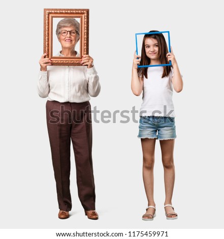 Full body of an elderly lady and her granddaughter smiling and relaxed, looking through a frame, funny and creative photo, concept of photography