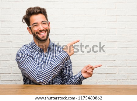 Young caucasian man sitting pointing to the side, smiling surprised presenting something, natural and casual