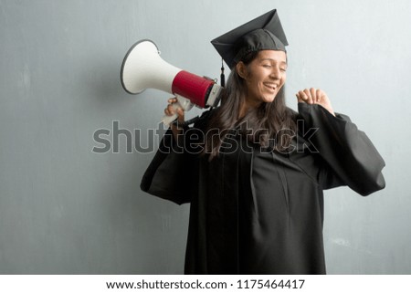 Young graduated indian woman against a wall Listening to music, dancing and having fun, moving, shouting and expressing happiness, freedom concept. Holding a megaphone.