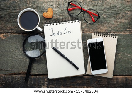 To do list in notepad with cup of coffee, smartphone and magnifying glass on grey wooden table