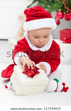 Baby girl in santa outfit opening a present sitting on the floor