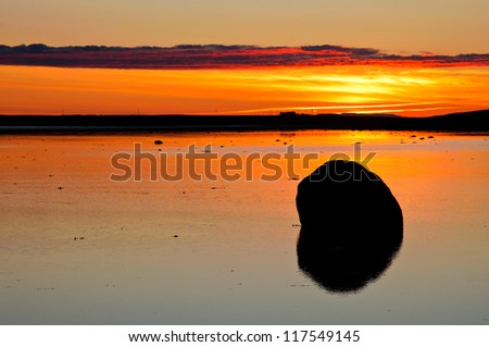 Alone rock inside the calm lake during amazing orange sunrise