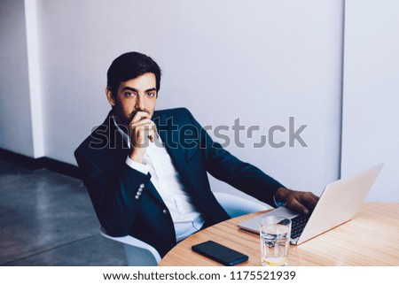 Experienced businessman spending time in workspace using laptop computer for planning and searching information for training with employees, thoughtful man wear in formal suit looking at camera